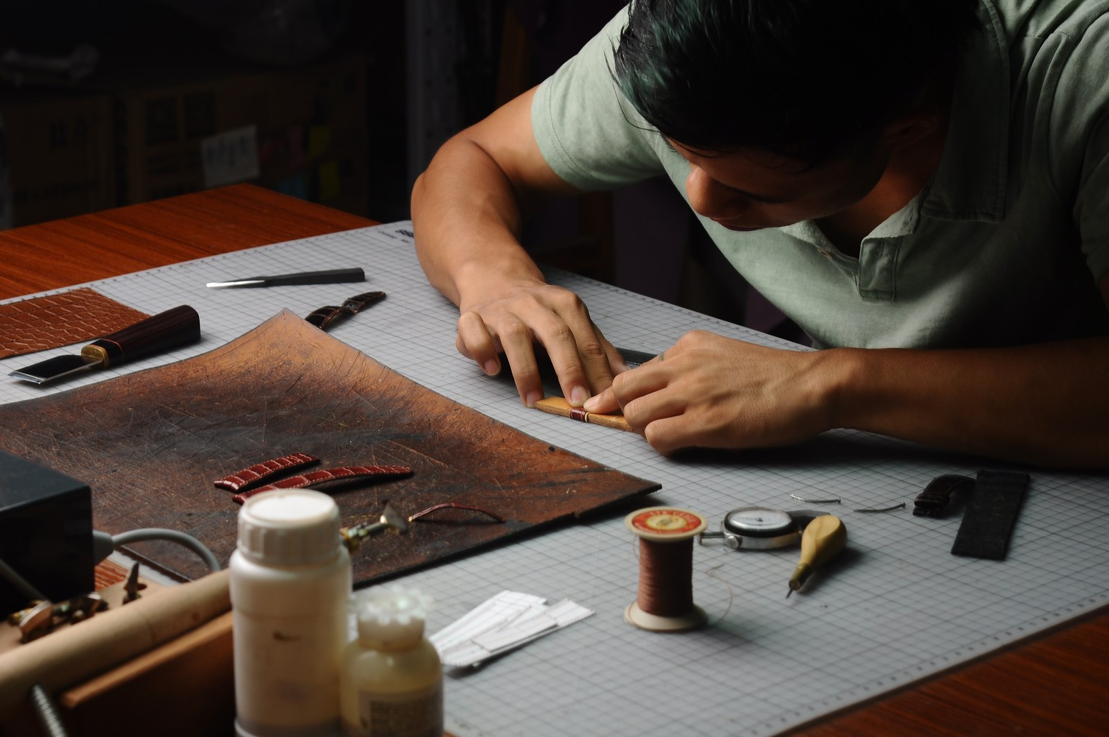 A maker working at a bench surrounded by brown leather, thread and hand tools