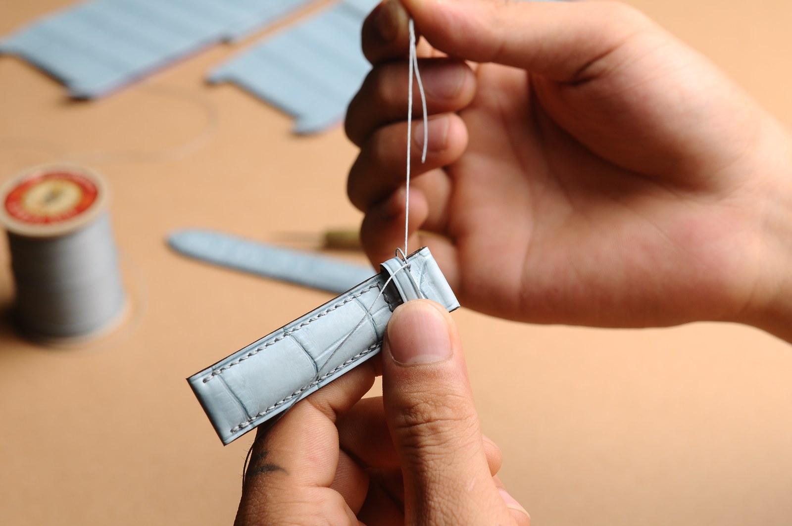 Hands guiding a real manual stitching step on a leather piece