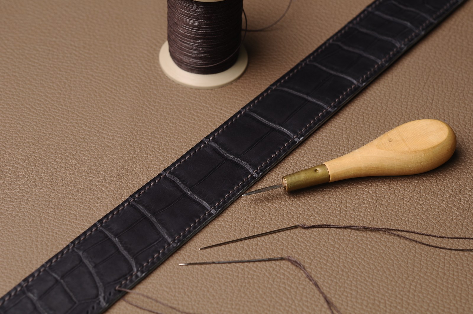 Black crocodile leather belt with brown lining, thread, needle and hand tools