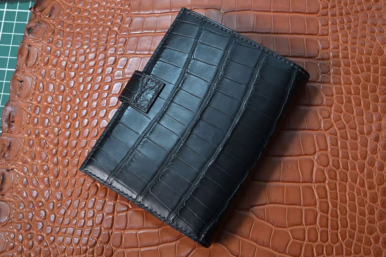 Closed black genuine crocodile leather passport cover with a short closure strap and edge stitching