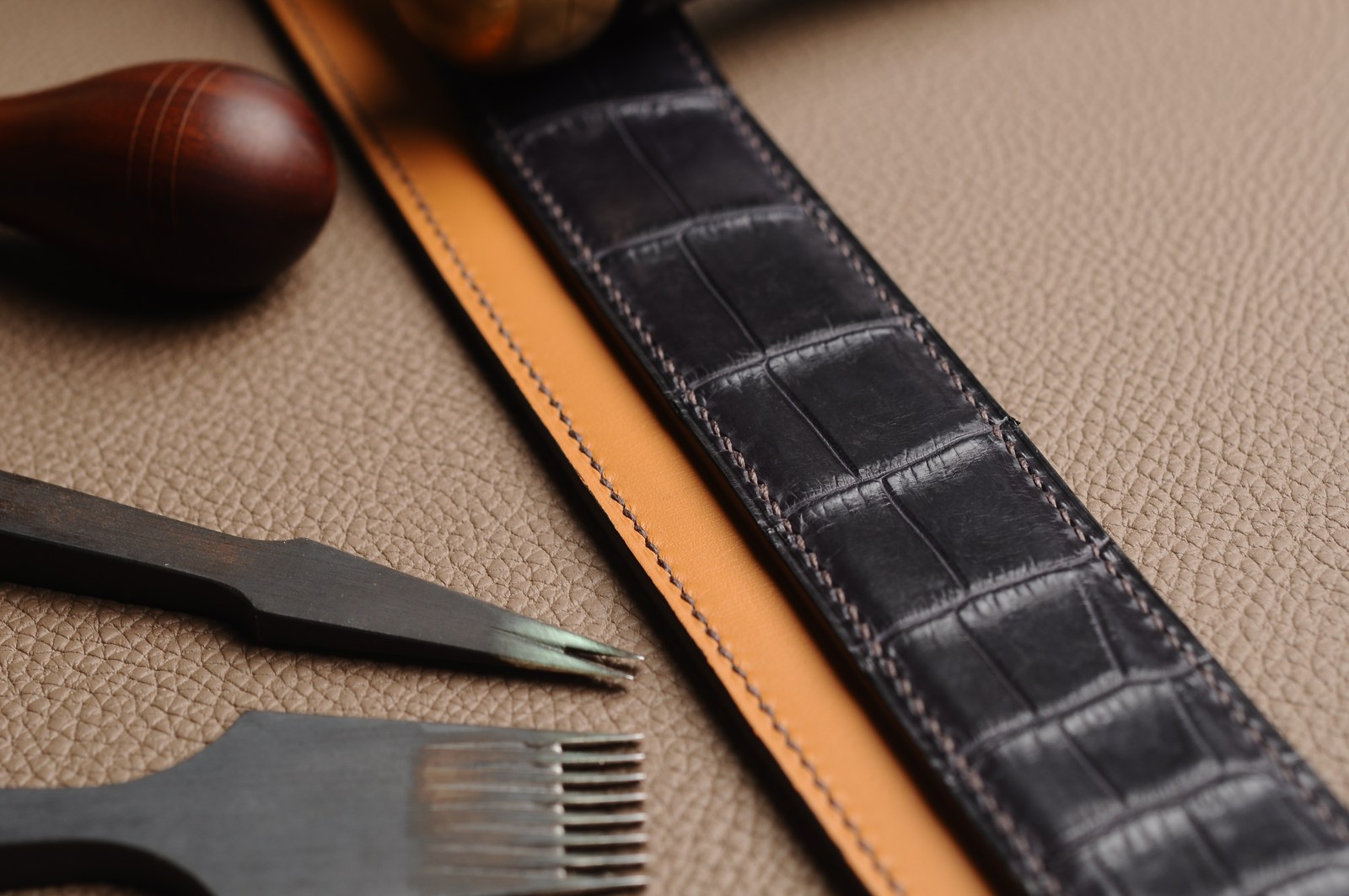 Black crocodile leather and brown lining belt components beside hand tools